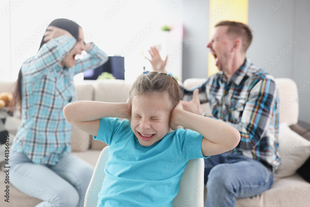 Little girl covering her ears with her hands against background of swearing parents at home Little girl covering her ears with her hands against background of swearing parents at home