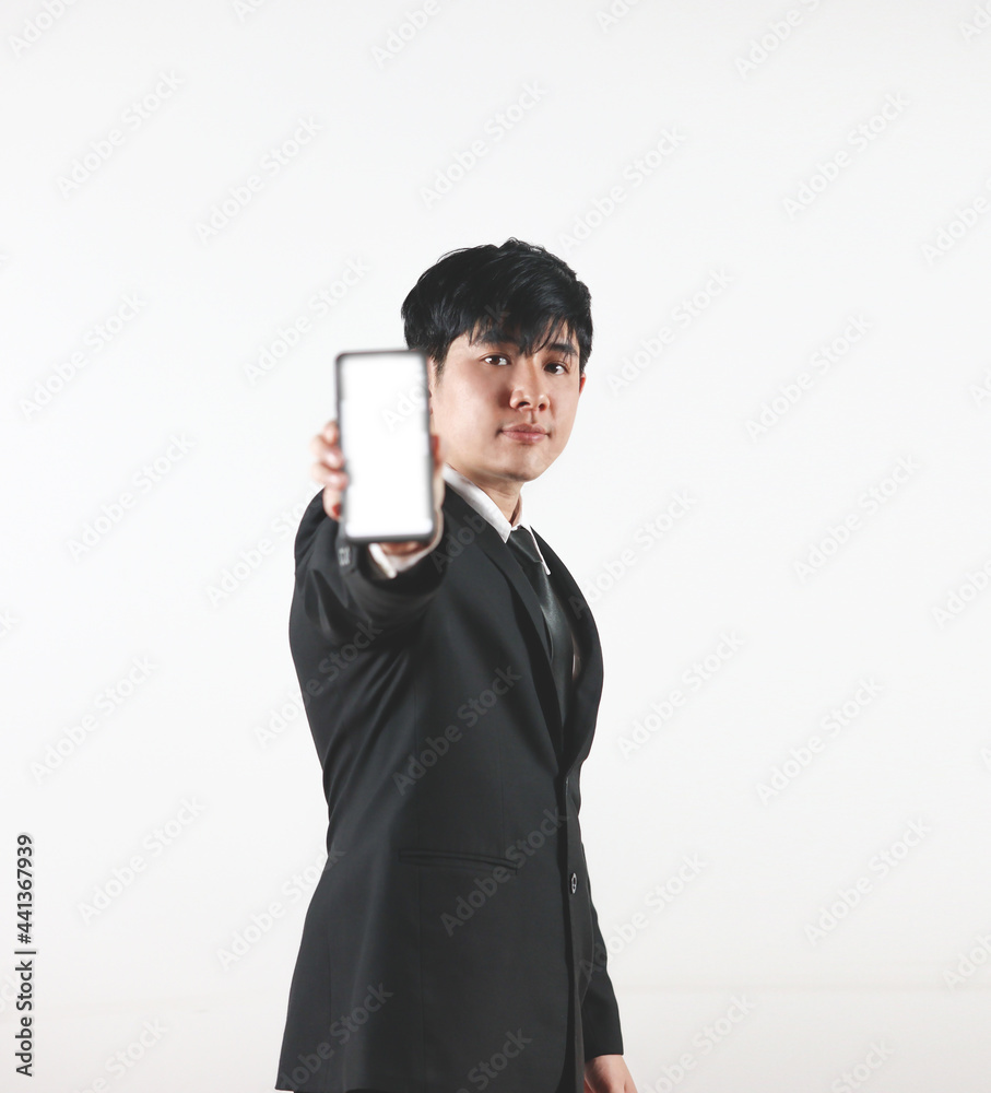 Asian man in a black suit standing and showing a blank screen smartphone on white background. Selective focus on people. Asian man in a black suit standing and showing a blank screen smartphone on white background. Selective focus on people.