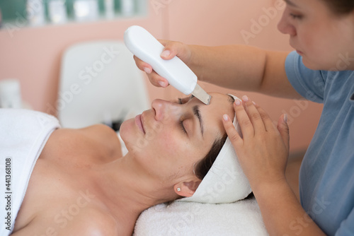 Ultrasonic skin cleaning procedure of face. Skin Care. Close-up of beautiful woman receiving ultrasound facial peeling. Beauty treatment and cosmetology in spa salon. photo