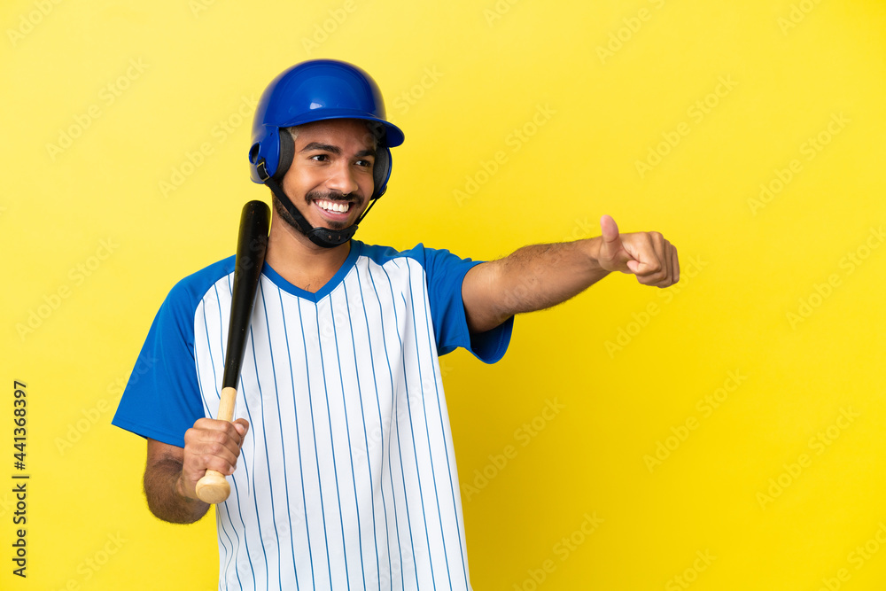 Young Colombian latin man playing baseball isolated on yellow background giving a thumbs up gesture