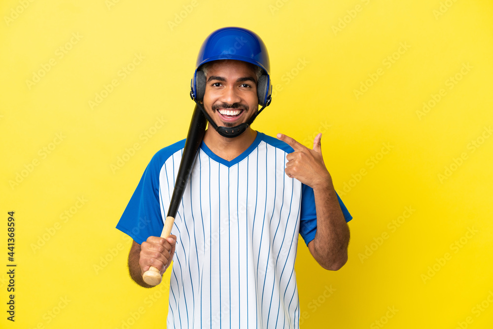 Young Colombian latin man playing baseball isolated on yellow background giving a thumbs up gesture Young Colombian latin man playing baseball isolated on yellow background giving a thumbs up gesture