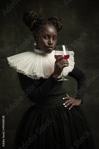 Portrait of medieval African young woman in black vintage dress with big white collar posing isolated on dark green background. Cheers