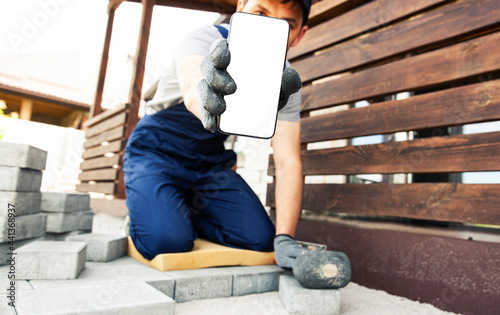 bricklayer holding the phone with blank screen in hand on gloves.  mockup for house repair or building © SkyLine