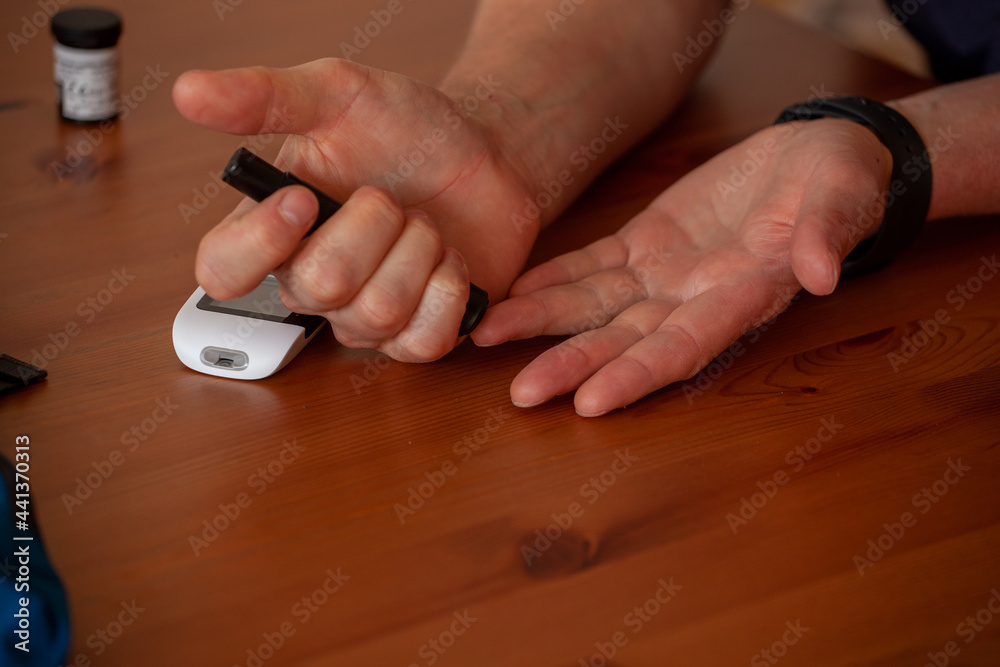 Un homme diabétique se pique pour connaître son taux de glycémie. Ses deux mains sont posées sur