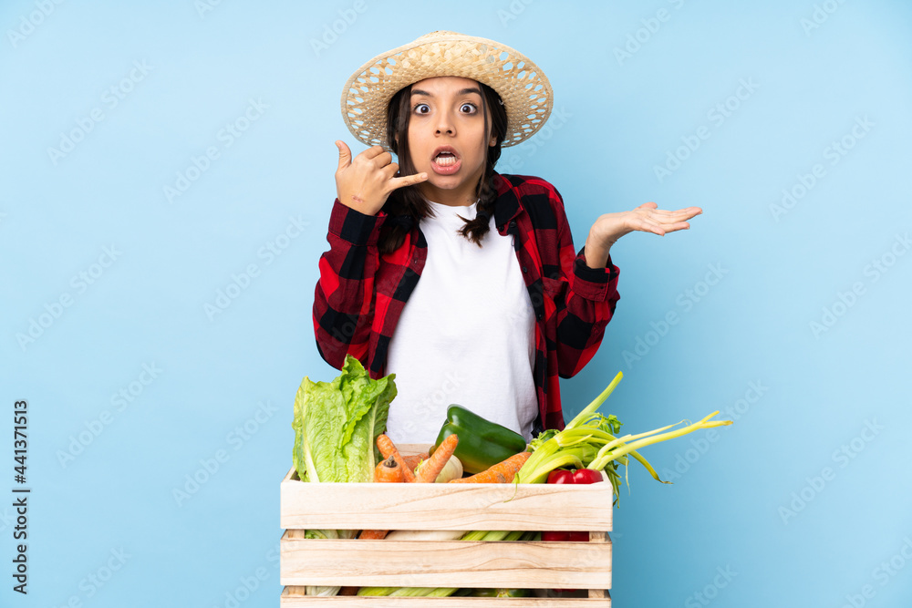 Young farmer Woman holding fresh vegetables in a wooden basket making phone gesture and doubting
