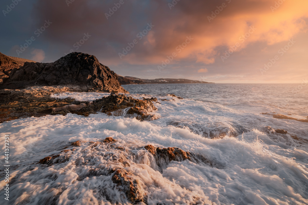 Waves of white foam cover the rocks on the Galdar coast at sunset. Gran Canaria. Canary Islands
