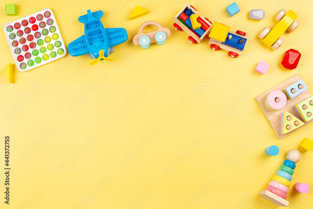 Baby kids toys background with wooden blocks, train, car, plane, pop it fidget toys on yellow background. Top view, copy space - obrazy, fototapety, plakaty 