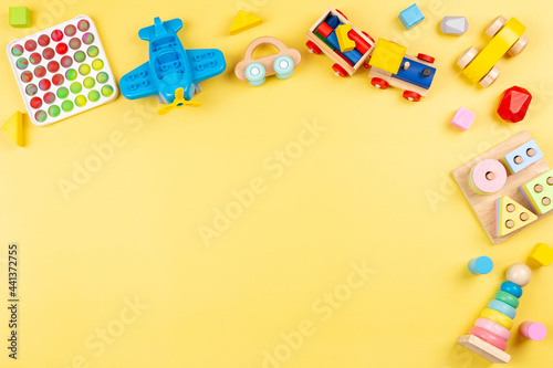 Baby kids toys background with wooden blocks, train, car, plane, pop it fidget toys on yellow background. Top view, copy space