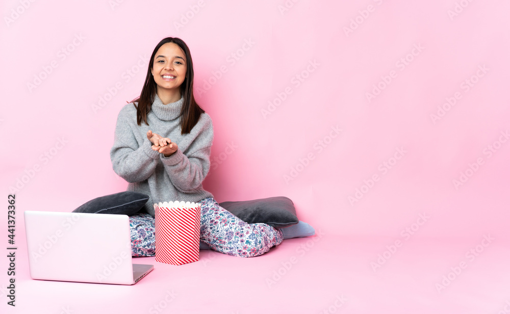 Young mixed race woman eating popcorn while watching a movie on the laptop holding copyspace imaginary on the palm to insert an ad Young mixed race woman eating popcorn while watching a movie on the laptop holding copyspace imaginary on the palm to insert an ad