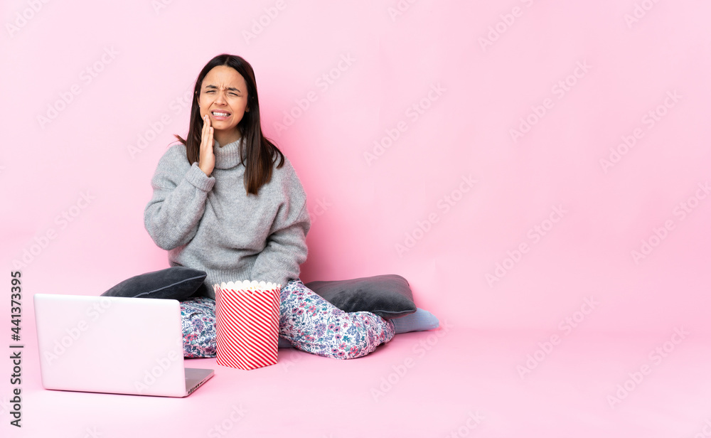 Young mixed race woman eating popcorn while watching a movie on the laptop with toothache Young mixed race woman eating popcorn while watching a movie on the laptop with toothache