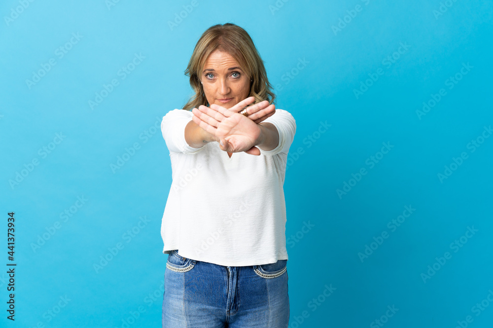 Middle aged blonde woman over isolated background making stop gesture with her hand to stop an act Middle aged blonde woman over isolated background making stop gesture with her hand to stop an act