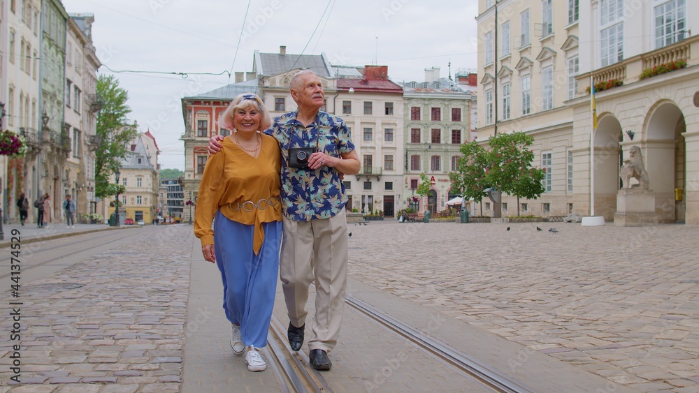 Senior stylish tourists man woman walking along street, looking for way using paper map in old town Lviv, Ukraine. Elderly travelers grandmother, grandfather getting lost in big city. Summer vacation