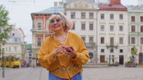 Elderly stylish tourist woman looking for way using smartphone in old town Lviv, Ukraine. Senior mature traveler grandmother pensioner getting lost in big city trying to find route. Summer vacation
