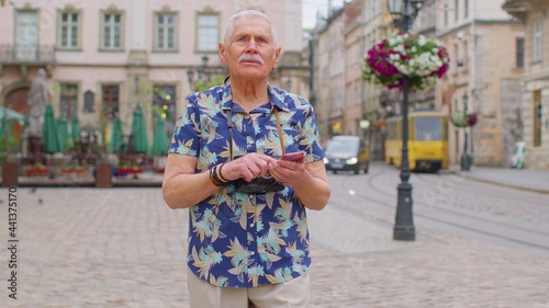 Elderly mature traveler guy grandfather pensioner getting lost in big city trying to find route. Senior stylish tourist man looking for way using smartphone in old town Lviv, Ukraine. Summer vacation