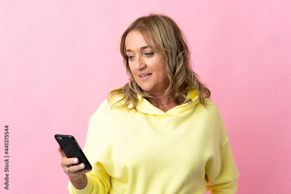 Middle aged blonde woman over isolated pink background sending a message or email with the mobile