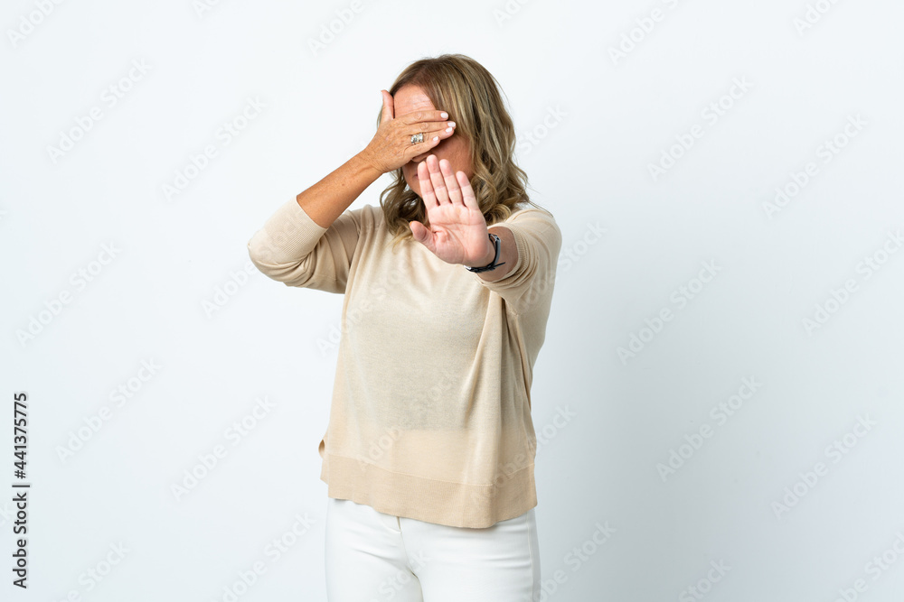 Middle aged blonde woman over isolated white background making stop gesture and covering face Middle aged blonde woman over isolated white background making stop gesture and covering face