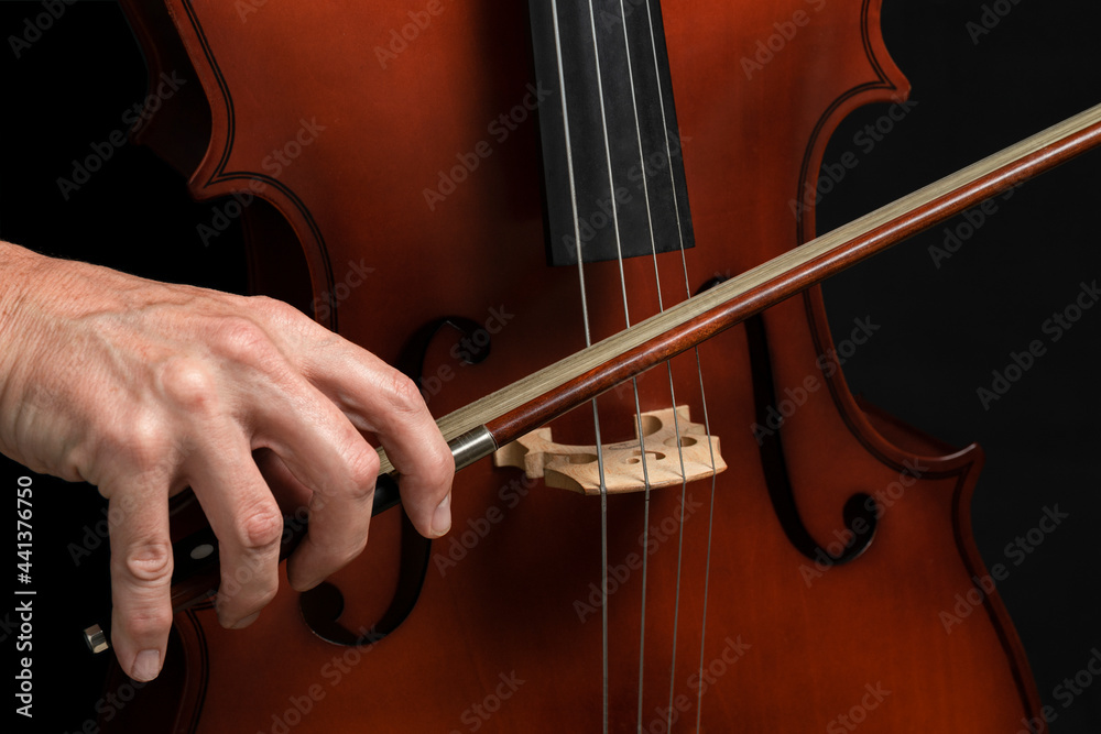 CLOSE UP OF MALE HAND PLAYING CELLO ON DARK BACKGROUND. CLOSE UP OF MALE HAND PLAYING CELLO ON DARK BACKGROUND.