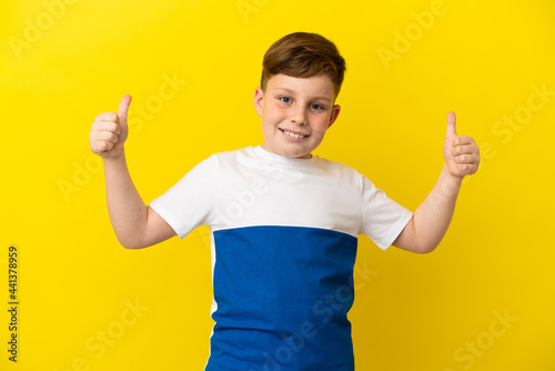 Little redhead boy isolated on yellow background giving a thumbs up gesture