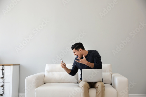 Emotional man with smartphone and laptop at home