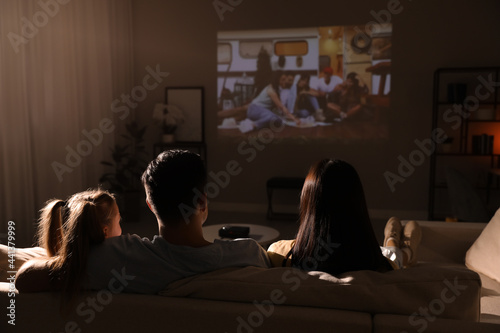 Family watching movie on sofa at night, back view