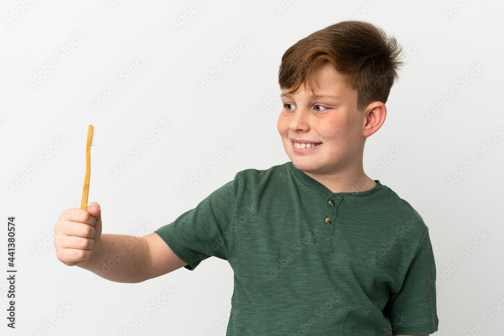 Little redhead boy holding a toothbrush isolated on white background with happy expression Little redhead boy holding a toothbrush isolated on white background with happy expression