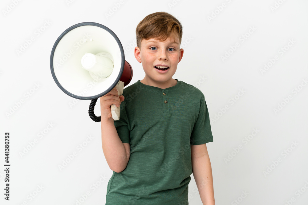 Little redhead boy isolated on white background holding a megaphone and with surprise expression Little redhead boy isolated on white background holding a megaphone and with surprise expression