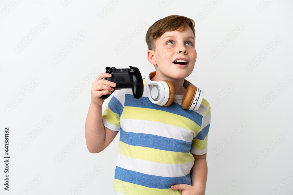 Little redhead boy holding a game pad isolated on white background looking up and with surprised expression Little redhead boy holding a game pad isolated on white background looking up and with surprised expression