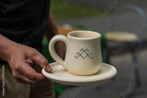 A white clay mug and a plate in the man's hand.