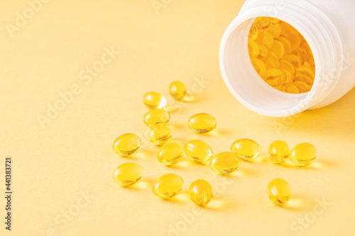 Transparent softgel capsules with fat-soluble vitamins and open plastic bottle on yellow background. Close-up, copy space.