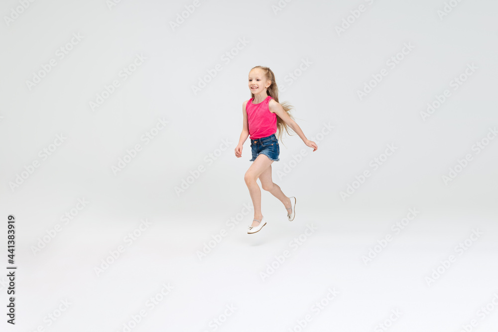 Beautiful little sportive girl in casual clothes running isolated on white studio background. Happy childhood concept.