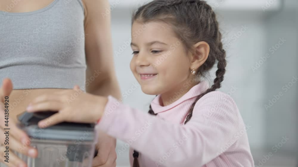 Cheerful cute Middle Eastern girl putting lemon in blender helping mother preparing healthful smoothie. Portrait of charming pretty daughter cooking with parent at home indoors Cheerful cute Middle Eastern girl putting lemon in blender helping mother preparing healthful smoothie. Portrait of charming pretty daughter cooking with parent at home indoors