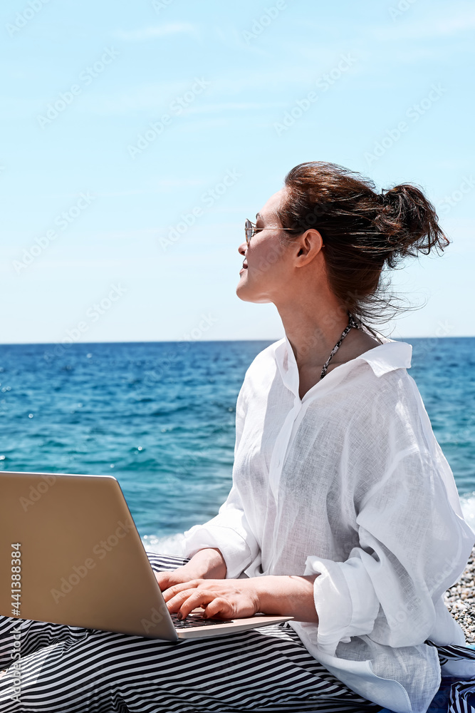 Successful pretty woman using laptop at the beach. Businesswoman working outdoors. Technology and travel, freelance concept.Modern office.Distant work