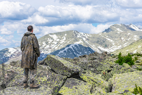 A man stands on a rock and looks towards the mountain peaks