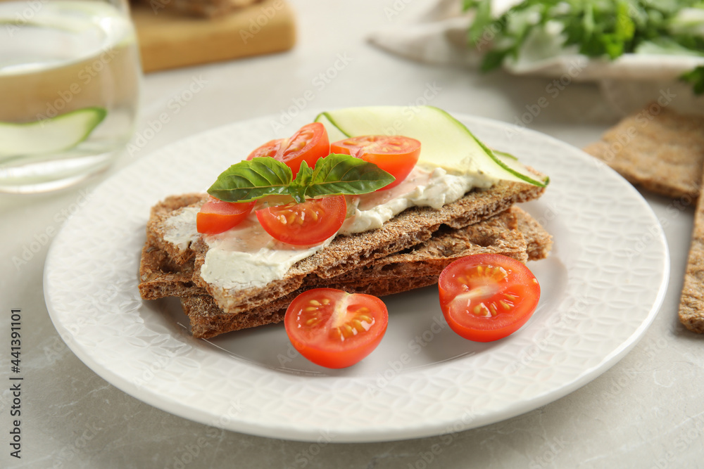 Fresh rye crispbreads with cream cheese and vegetables on light grey table, closeup