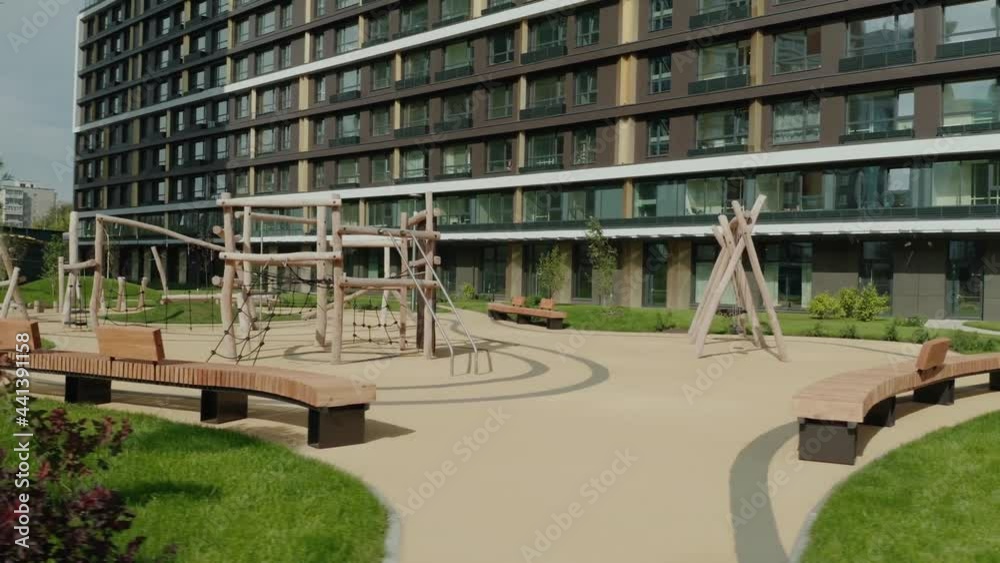 Summer landscape with empty modern playground in a new modern residential complex. Video. Children wooden playground with a multi storey house on the background.