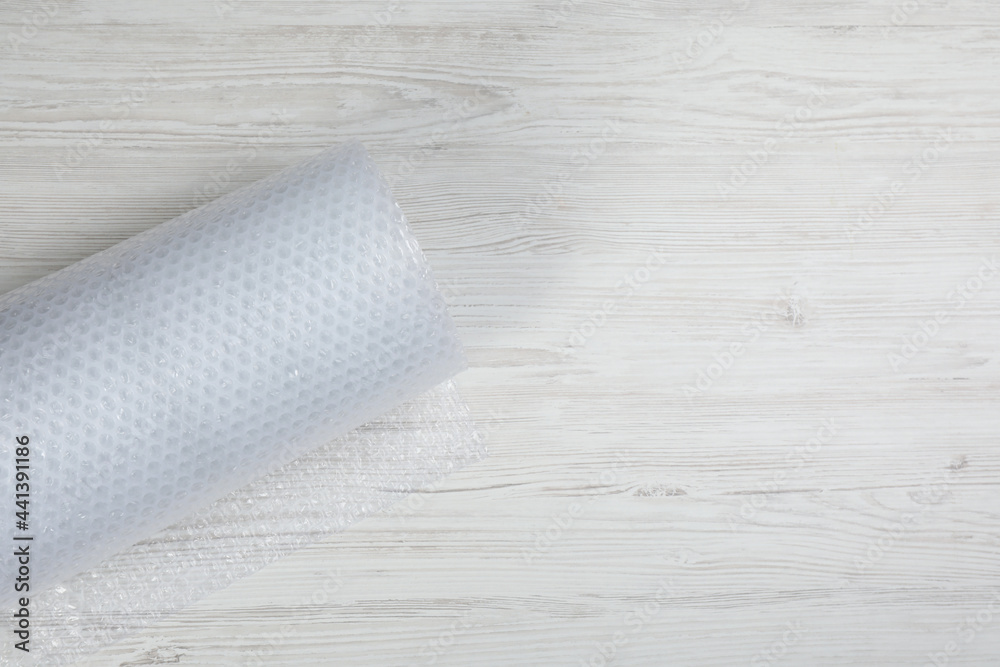 Fototapeta premium Bubble wrap roll on white wooden background, top view. Space for text