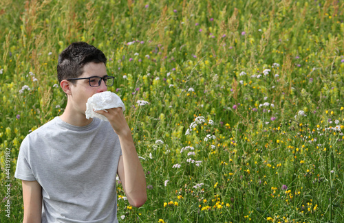 young boy with asthma sneezes on a handkerchief because of allergy to grass on flowery field in Spring