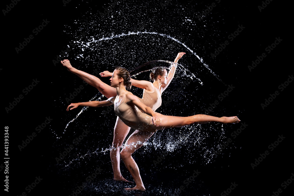 Couple of athletic women are doing dancing tricks under streams, splashes, drops of rain water. Duo acrobats, ballet dancers are performing dance. Freedom and freshness concept. Modern art and beauty.