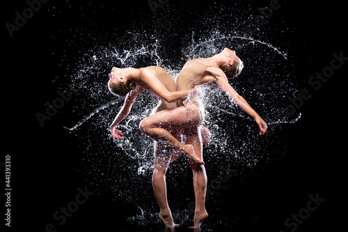 Couple of athletic women are doing dancing tricks under streams, splashes, drops of rain water. Duo acrobats, ballet dancers are performing dance. Freedom and freshness concept. Modern art and beauty.