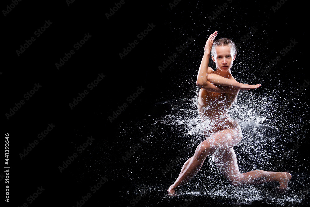 Wet young woman in tight beige swimsuit is dancing on floor under rain and splashes, drops of water. Girl modern dancer is doing tricks. Contemporary art dance. Freedom and freshness concept.