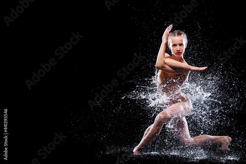 Wet young woman in tight beige swimsuit is dancing on floor under rain and splashes, drops of water. Girl modern dancer is doing tricks. Contemporary art dance. Freedom and freshness concept.
