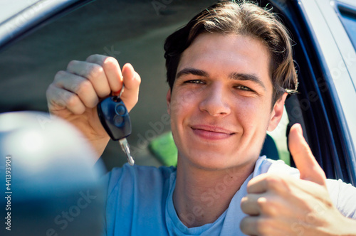 Smiling young driver showing new car keys and car.