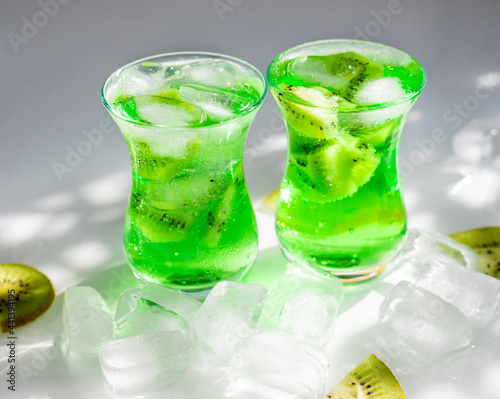 Green lemonade with ice and kiwi slices.Two glass glasses stand on the table and the sun's rays fall on them.