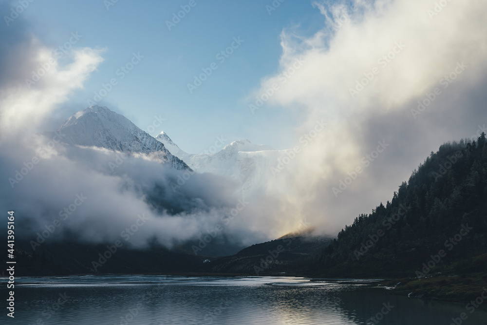 Beautiful view of snow-capped mountains above thick clouds in sunshine. Scenic mountain landscape with white-snow peak among dense low clouds in blue sky. Wonderful alpine scenery with snowy pinnacle. Beautiful view of snow-capped mountains above thick clouds in sunshine. Scenic mountain landscape with white-snow peak among dense low clouds in blue sky. Wonderful alpine scenery with snowy pinnacle.