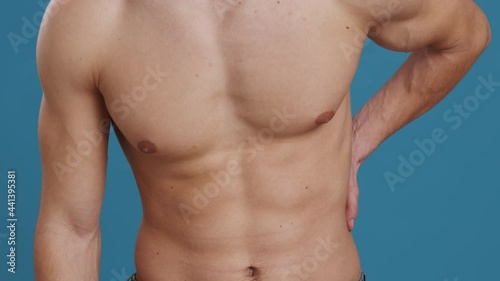 Kidney pain. Young unrecognizable caucasian man touching his lower back, suffering from acute pain, blue background photo