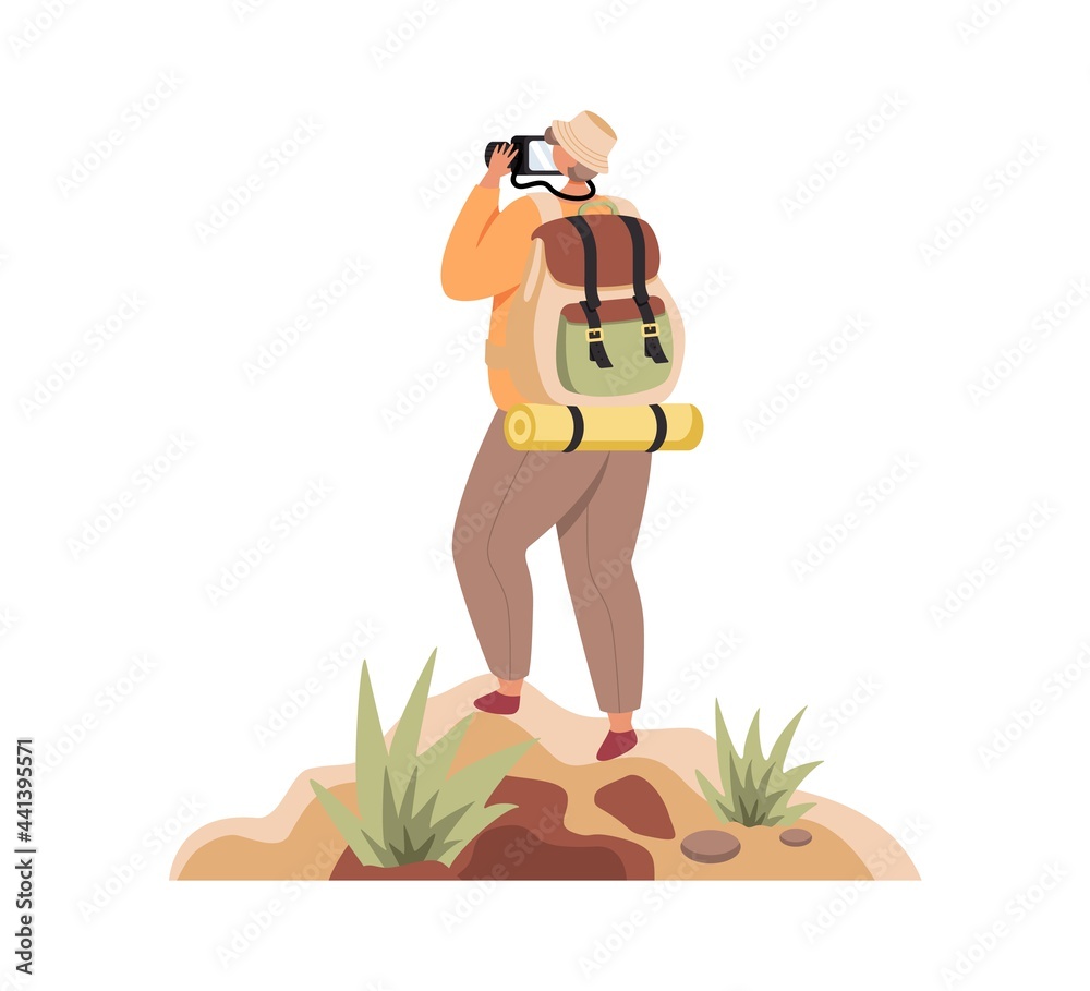 Traveller with backpack standing on top of mountain and looking through camera.