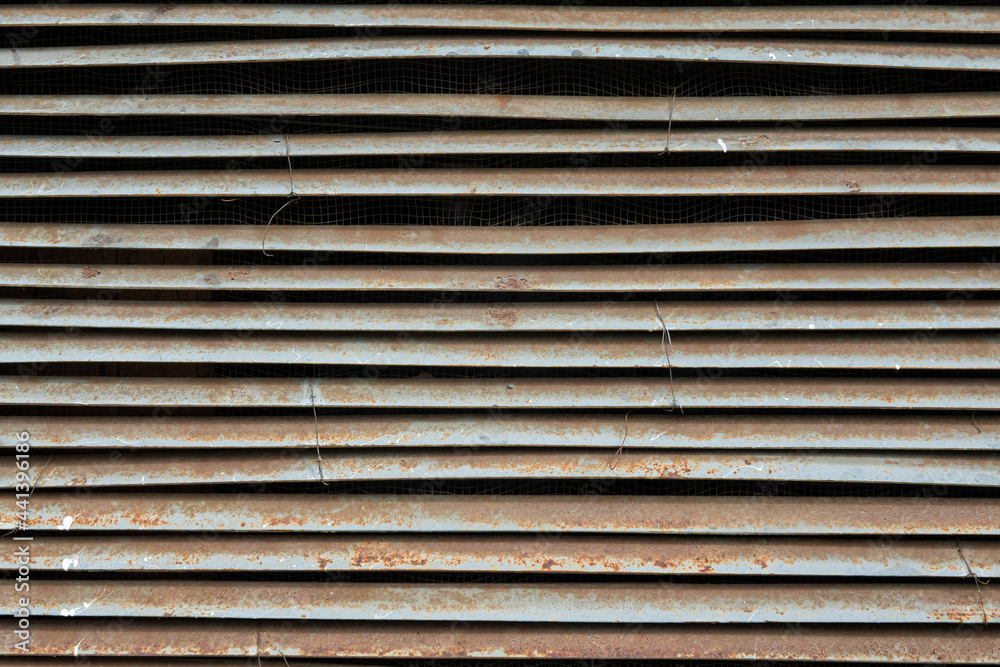Close-up of an old industrial ventilation window. The gray steel elements of the louver are curved and the surface is corroded. Background. Texture. Close-up of an old industrial ventilation window. The gray steel elements of the louver are curved and the surface is corroded. Background. Texture.