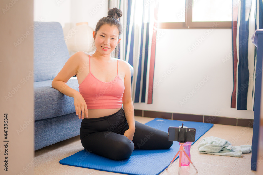 home lifestyle portrait of young happy and beautiful Asian Korean woman sweaty after training workout on yoga mat following online lesson on her mobile phone home lifestyle portrait of young happy and beautiful Asian Korean woman sweaty after training workout on yoga mat following online lesson on her mobile phone
