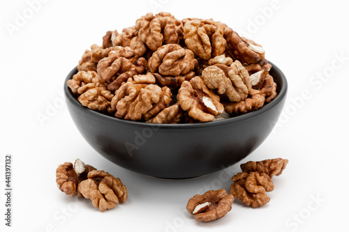 Walnuts in a bowl and a few nuts scattered around on a white background. Template for designers.