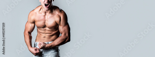 Muscular male strains muscles and screams. Muscular bodybuilder posing over white background. Muscular man screaming. Screaming man with well trained body, biceps, abs and pecs and wearing